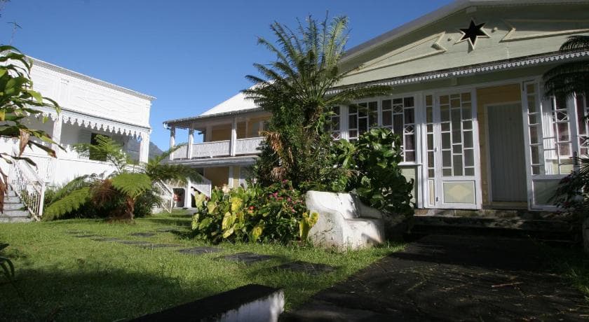 Entrée du Relais des Cimes à Hell-Bourg, allée pavée, bancs blancs et jardin tropical devant la case