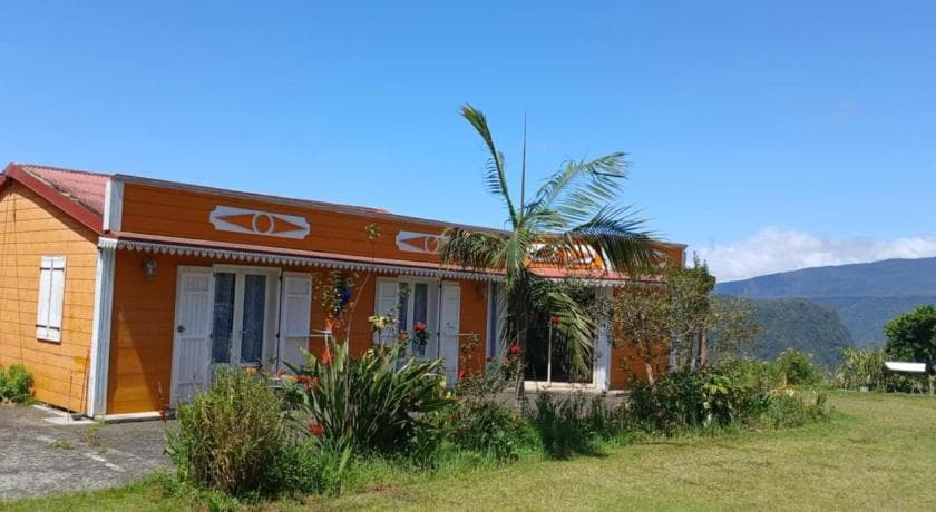 Case créole orange de la chambre d'hôtes Chez Nou à Grand Îlet, jardin et palmier sous un ciel bleu
