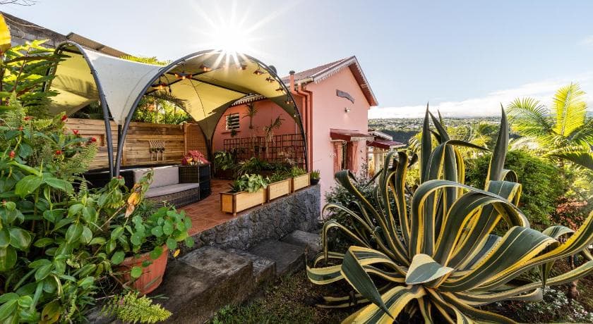 The pink Le Quéléa house, a shaded terrace, planters and a large agave in the foreground