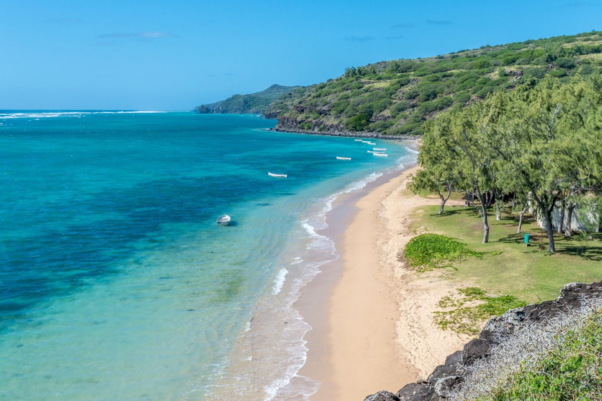 Plage déserte de l'île Rodrigues avec sable doré, lagon turquoise et collines verdoyantes, ambiance préservée des Mascareignes