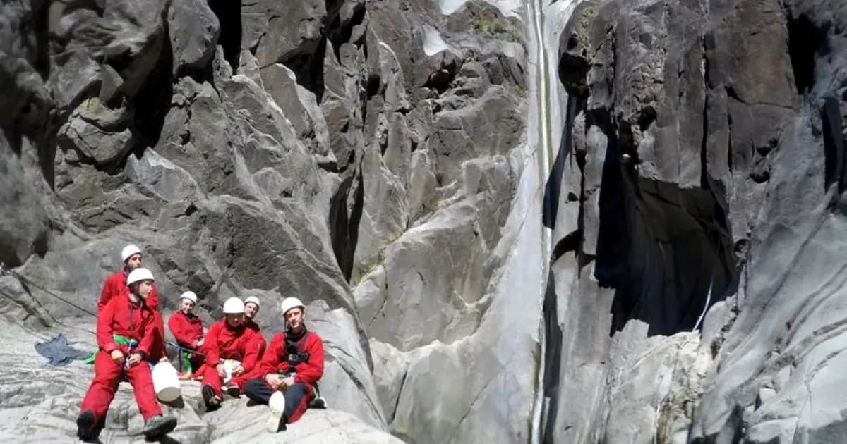 Groupe de canyoneurs en combinaisons rouges au pied de la grande paroi du canyon Fleur Jaune à Cilaos