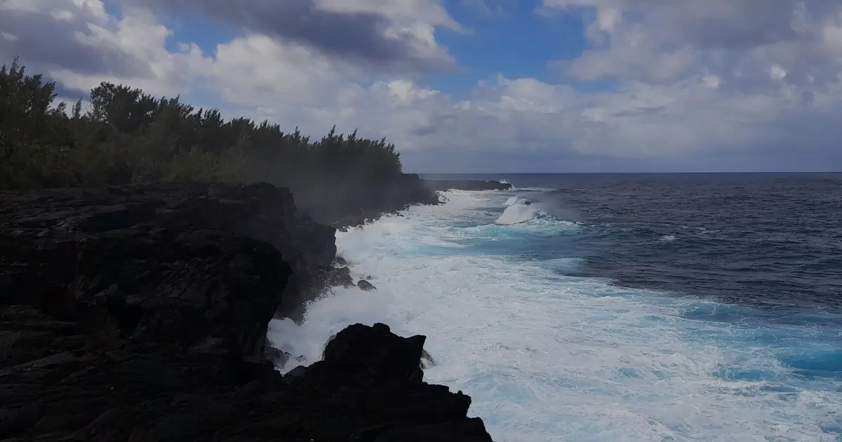 Black lava rocks under the spray near Puits Arabe, white waves along the Saint-Philippe coast