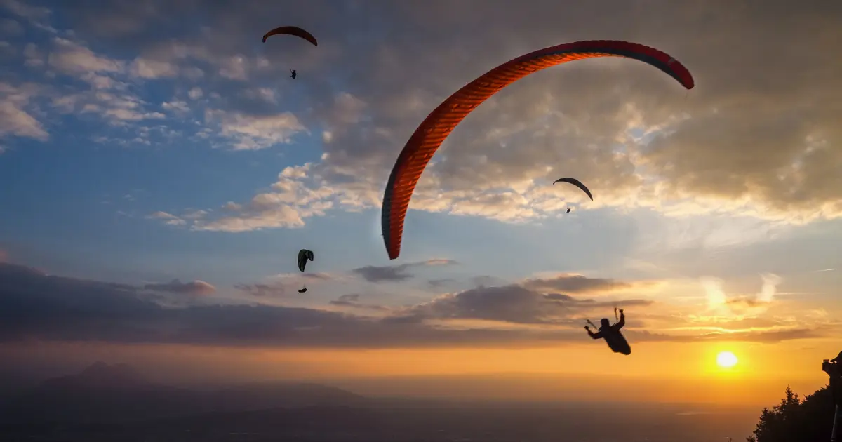 Parapentes en silhouette au coucher du soleil au-dessus de la côte ouest de La Réunion : activité aérienne typique à réserver à l'avance