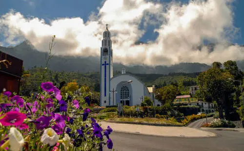 Église Notre-Dame-des-Neiges à Cilaos avec fleurs et montagnes en arrière-plan