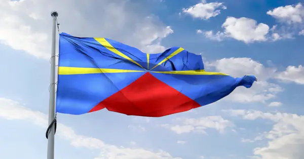The Mavéli or Radiant Volcano flag of Reunion Island flying against a blue sky: a blue field, a fan of yellow rays, and a red triangle symbolising Piton de la Fournaise