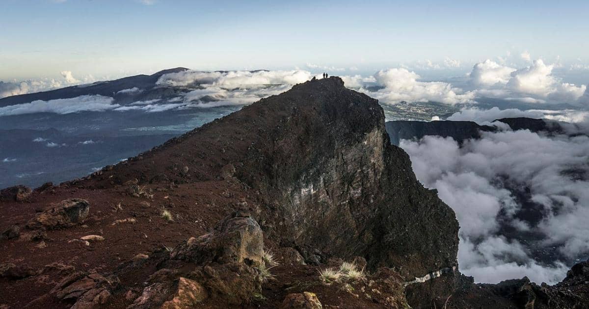 The summit ridge of Piton des Neiges at sunrise, two hikers at the top, a sea of clouds all around