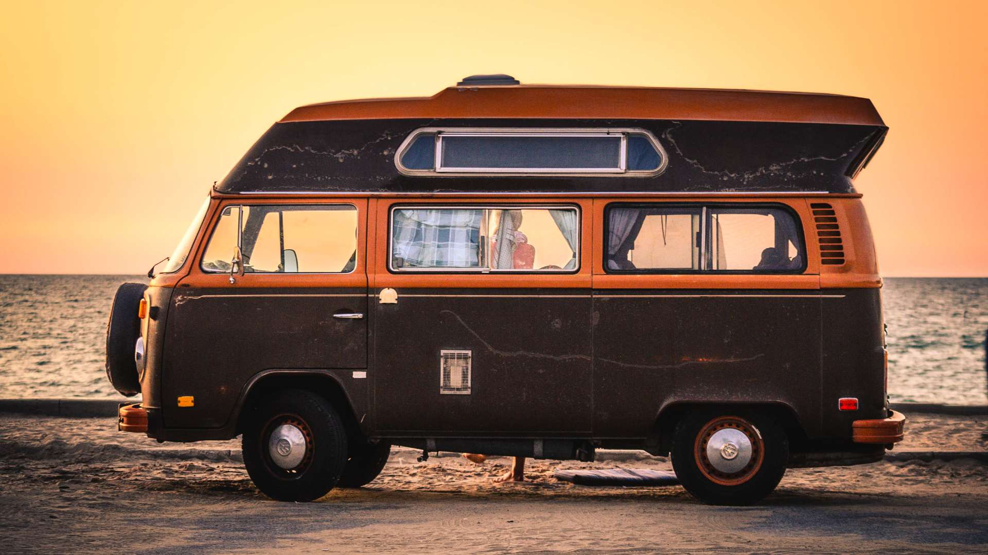 Combi Volkswagen brun garé face à l'océan au coucher du soleil, ambiance road trip en autonomie