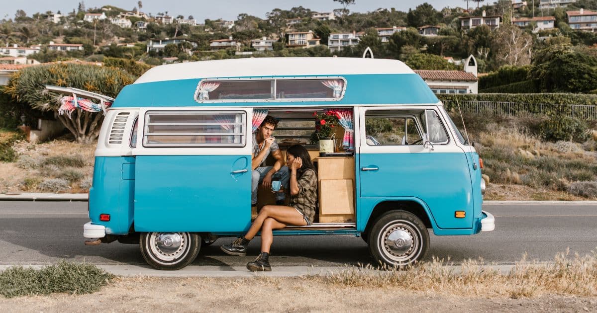 Combi Volkswagen bleu et blanc avec couple installé dans l'ouverture latérale, sur une route côtière