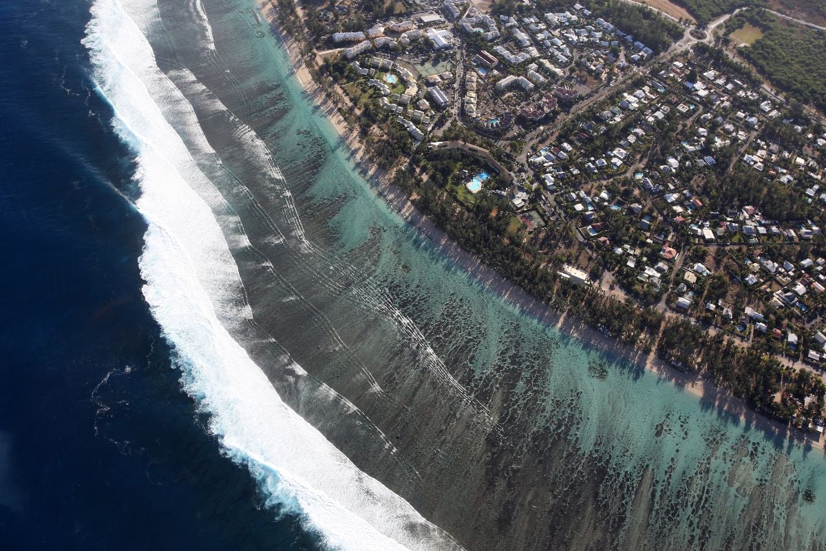 Vue aérienne du littoral ouest de La Réunion : lagon turquoise, barrière de corail, bord de mer urbanisé, témoin de l'intégration du DROM à la République