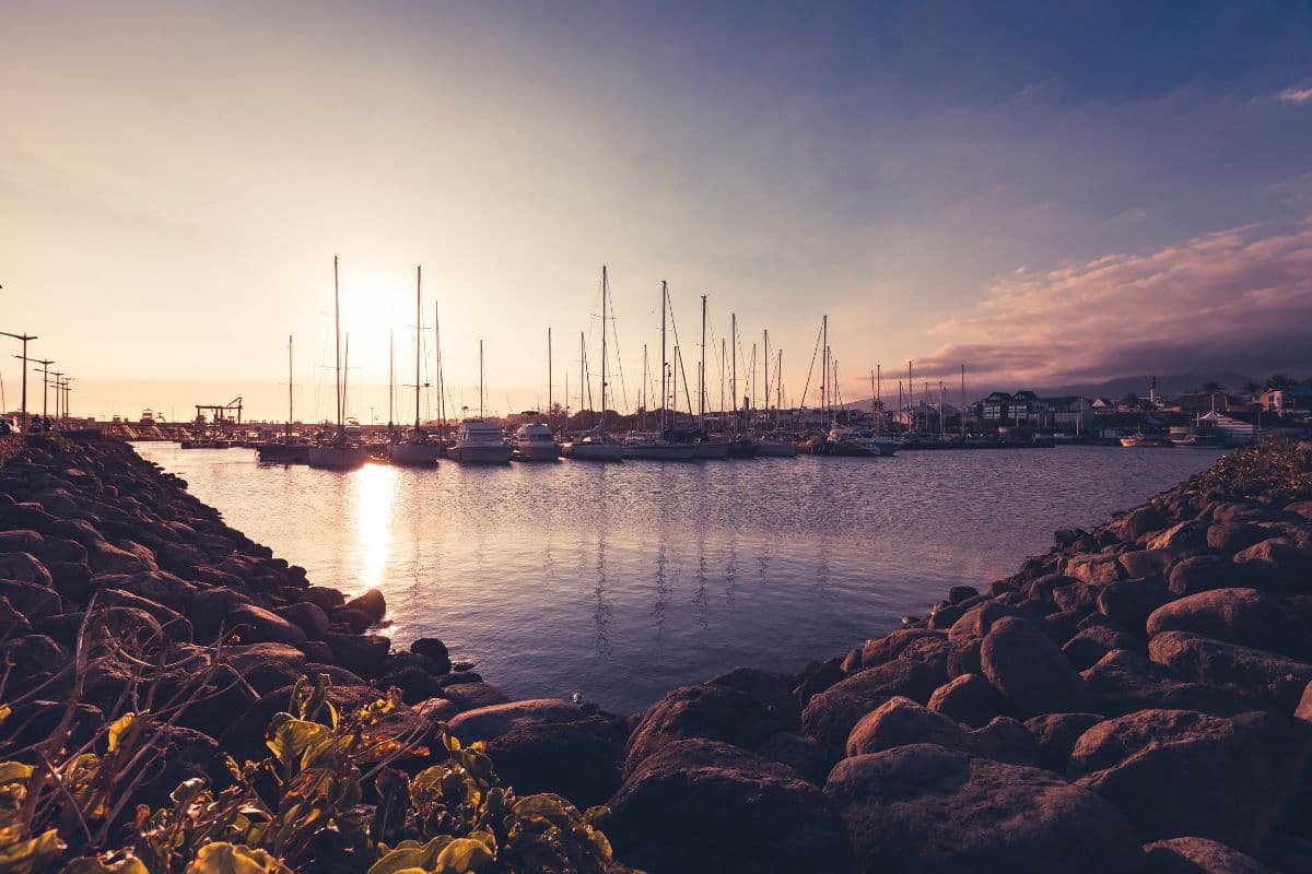 Port de plaisance de Saint-Pierre au coucher du soleil, voiliers alignés et reflets dorés sur l'eau depuis la digue de galets
