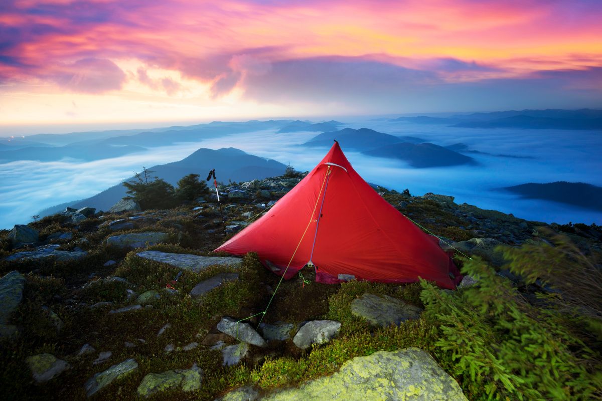 Tente de randonnée rouge plantée sur une crête rocheuse au-dessus d'une mer de nuages au crépuscule