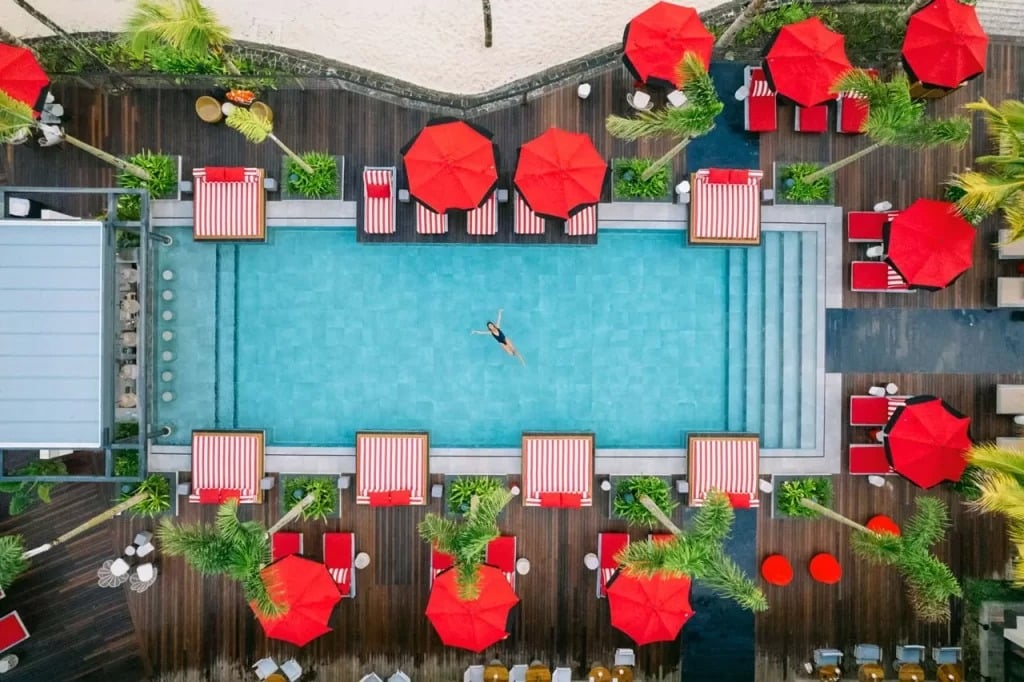 Vue aérienne d’une piscine d’hôtel rectangulaire avec parasols rouges et terrasse en bois