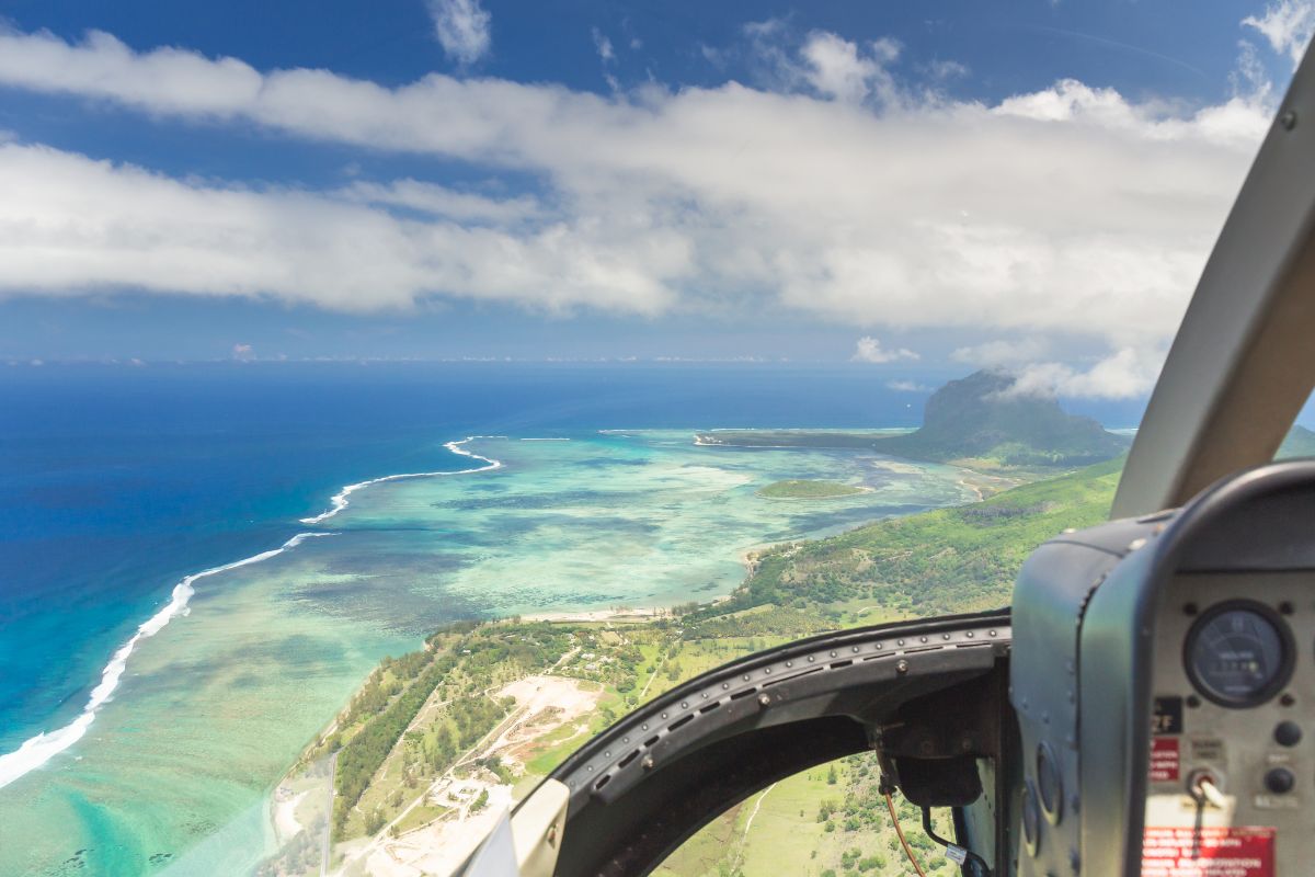 View from a helicopter cockpit flying over turquoise lagoons and the Le Morne Brabant peninsula in Mauritius