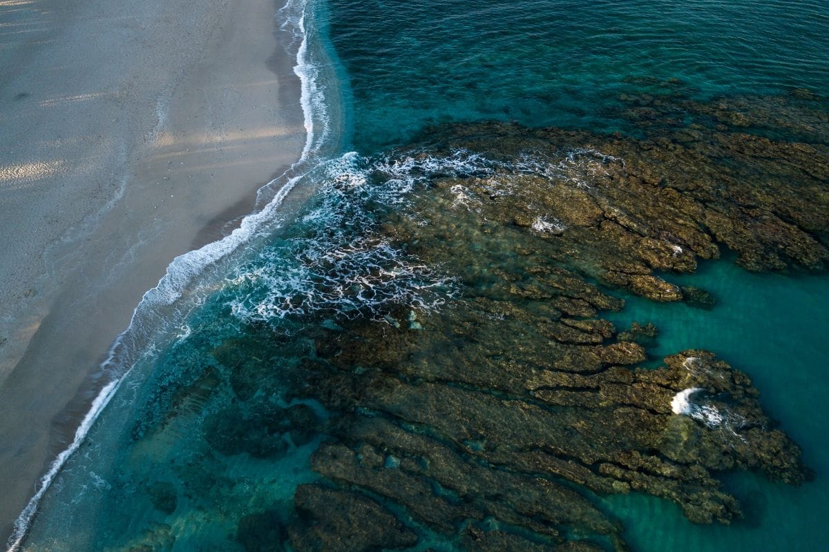 Vue aérienne de la barrière de corail de La Réunion avec la plage de sable clair, l'écume sur le récif et le lagon turquoise