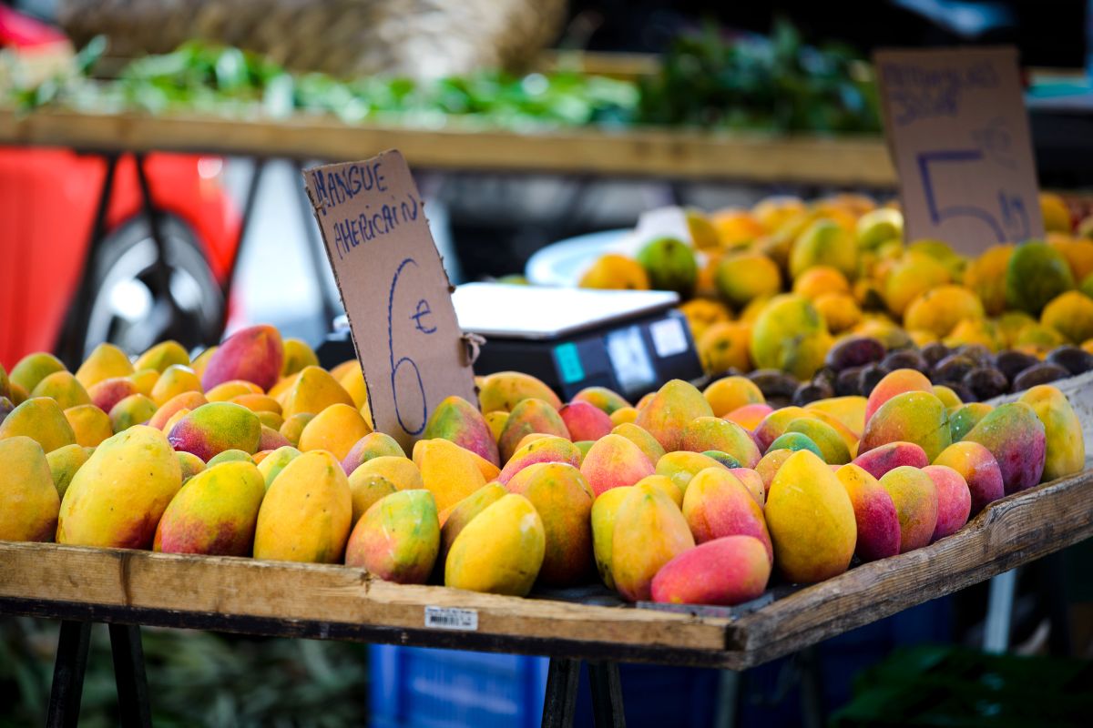 Étal de mangues mûres jaune et orange au marché forain de Saint-Paul, panneau cartonné « 6 € » manuscrit, illustration directe du coût des courses au quotidien à La Réunion