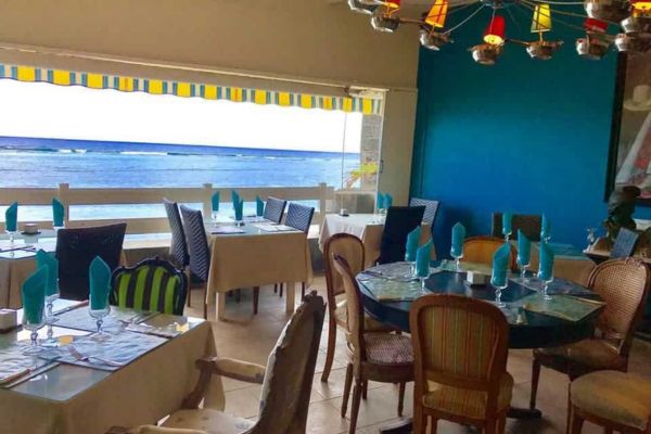 Salle de restaurant ouverte sur le lagon, déco bleu turquoise, tables dressées avec serviettes jaunes et bleues