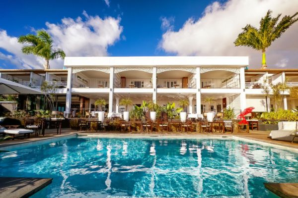 Hôtel-restaurant créole haut de gamme avec piscine au premier plan, façade blanche et palmiers