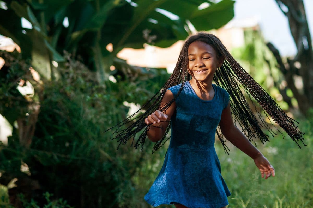Petite fille souriante aux tresses tournoyant dans un jardin tropical réunionnais bordé de bananiers