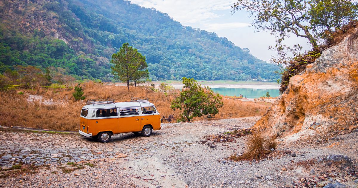 Van orange Volkswagen vintage stationné devant un lac et des montagnes, parfait pour un road-trip
