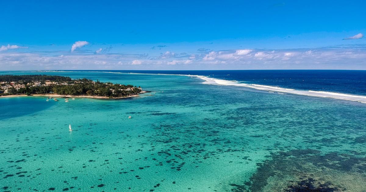 Vue aérienne du parc marin de Blue Bay, lagon turquoise, pointe boisée bordée de maisons et barrière de corail au large