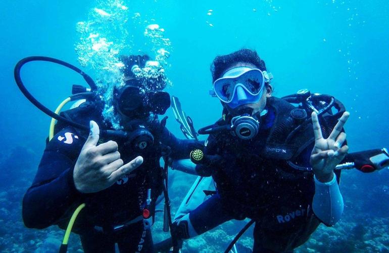 Deux plongeurs souriants sous l'eau, masques et détendeurs, dans une eau turquoise