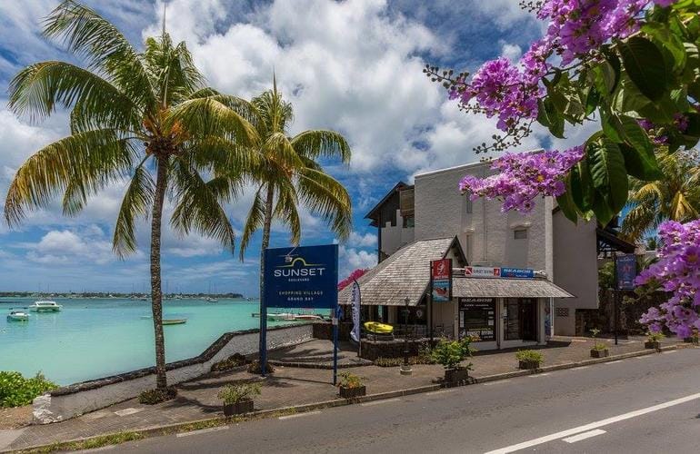 Route côtière de Grand Baie bordée de cocotiers et de bougainvilliers, le lagon et ses bateaux de l'autre côté du muret