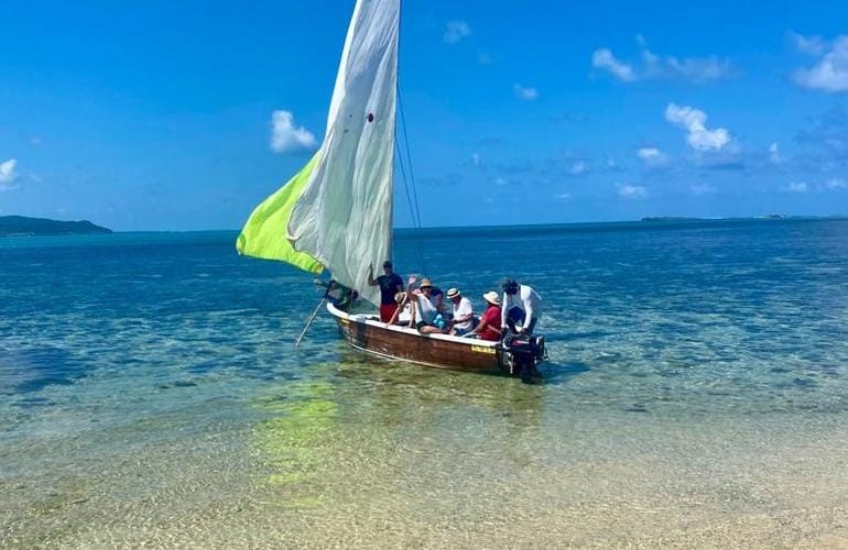 Pirogue à voile chargée de passagers dans l'eau peu profonde et transparente d'un lagon