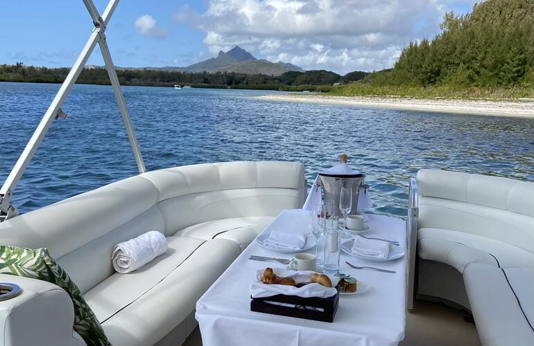 Table dressée sur un bateau à fond plat au mouillage, face à un banc de sable et à une côte boisée