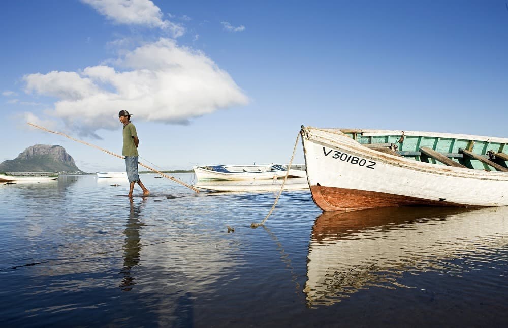 Pêcheur tirant sa barque dans un lagon de la côte ouest de Maurice, le Morne Brabant à l'horizon