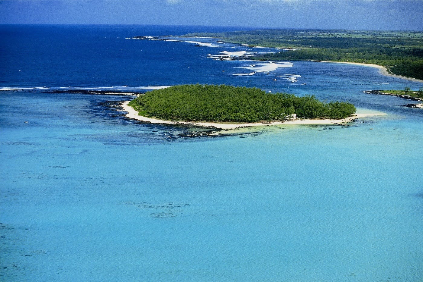 Vue aérienne d'un îlot boisé bordé de sable blanc dans un lagon turquoise