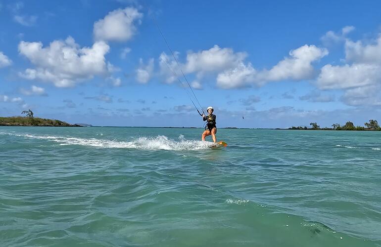 A kitesurfer gliding across a turquoise lagoon, low islets on the horizon