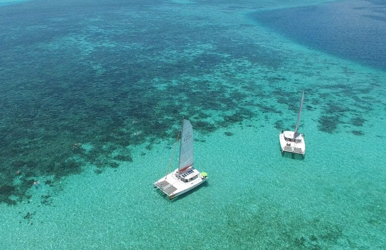 Deux catamarans au mouillage dans un lagon turquoise, au-dessus des massifs de corail