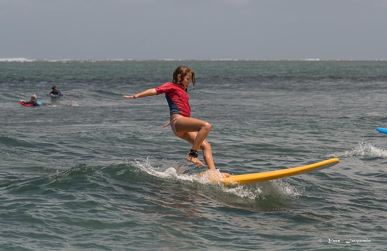 Cours de surf débutant à La Réunion, jeune surfeuse en équilibre sur une planche jaune