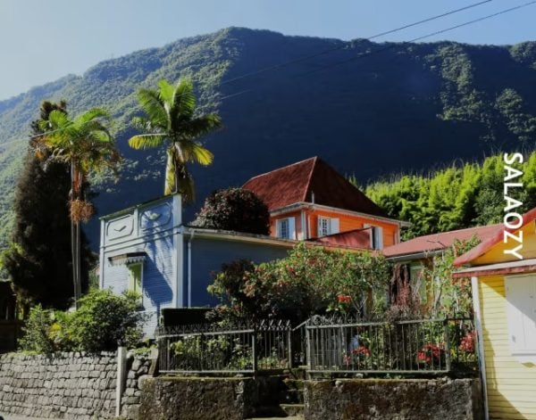 Maisons créoles colorées du village de Hell-Bourg avec montagne verdoyante en arrière-plan, panneau Salaozy à droite