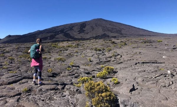 Randonneuse sur les pentes du Piton de la Fournaise avec champ de lave noir et sommet au loin