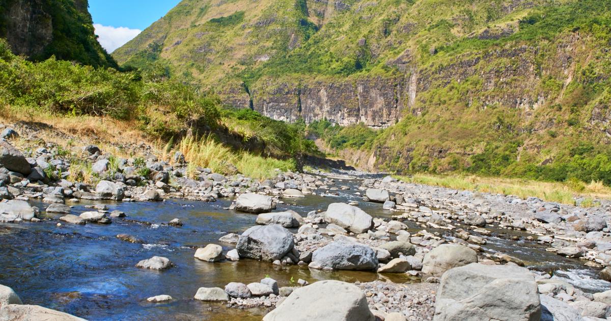 Rivière du sud sauvage à La Réunion en décembre, lit rocheux et montagnes verdoyantes sous un ciel d'été austral