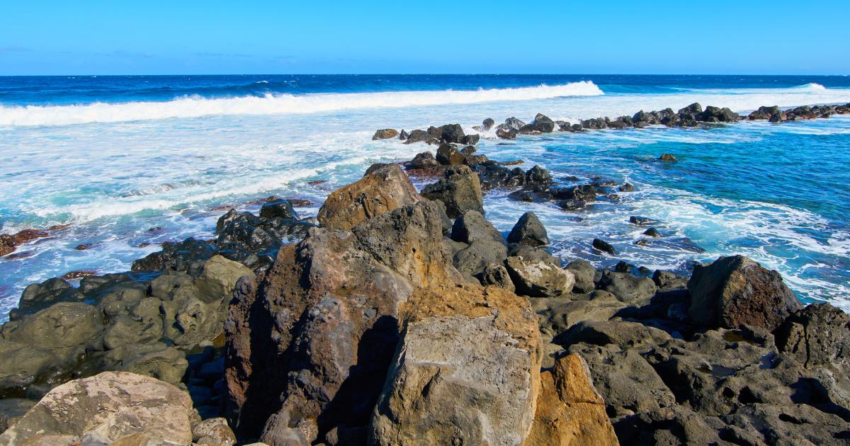 Côte rocheuse basaltique de La Réunion en octobre, rochers volcaniques et vagues sous un ciel bleu d'hiver austral