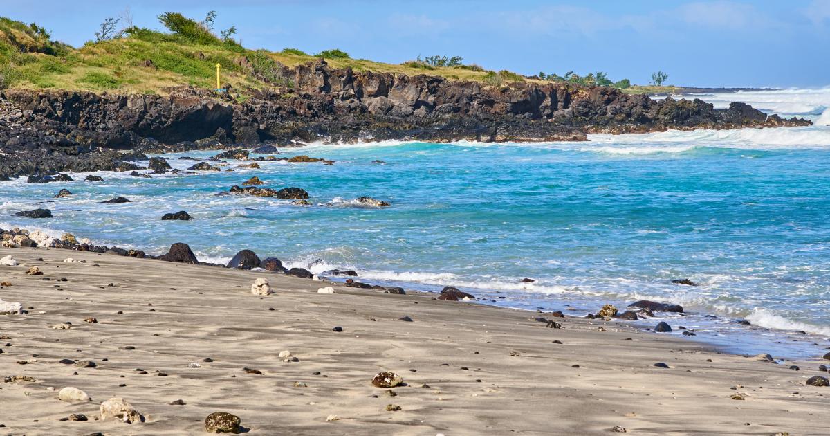 Plage de sable noir et rochers de basalte de la côte sauvage de La Réunion en juin, mer turquoise et alizés soutenus