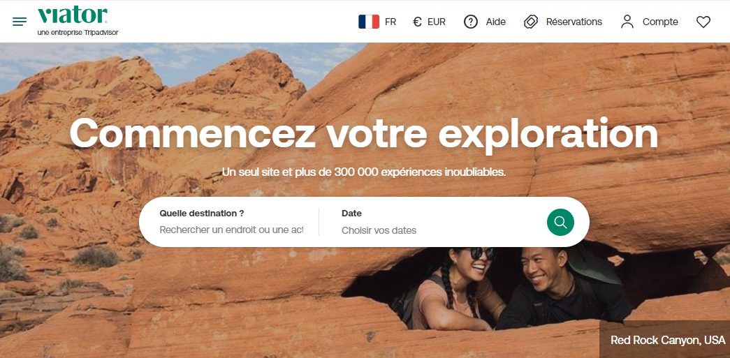 Page d'accueil Viator avec couple souriant dans une grotte de grès rouge de Red Rock Canyon aux USA, accroche Commencez votre exploration, un seul site et plus de 300 000 expériences inoubliables, barre de recherche destination et dates