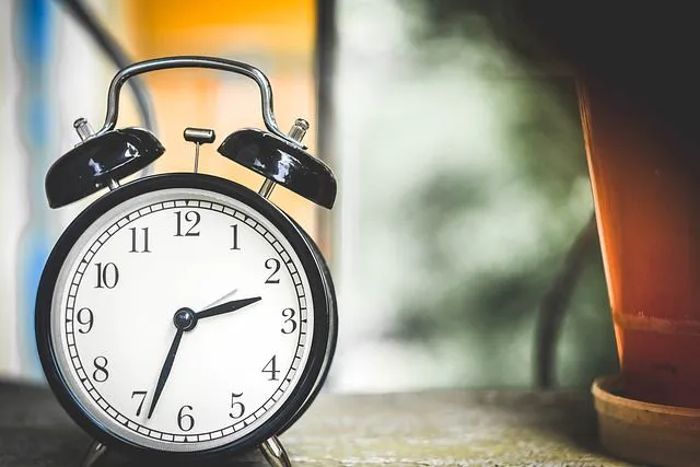 A classic alarm clock with hands showing the time and a glass of tea on a windowsill, a morning atmosphere