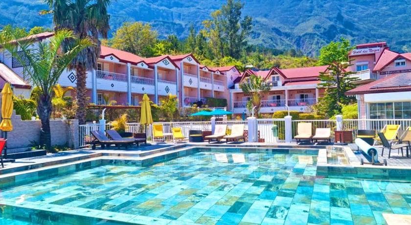 The pool at Hôtel des Neiges in Cilaos, yellow sunloungers and red-roofed buildings facing the mountains
