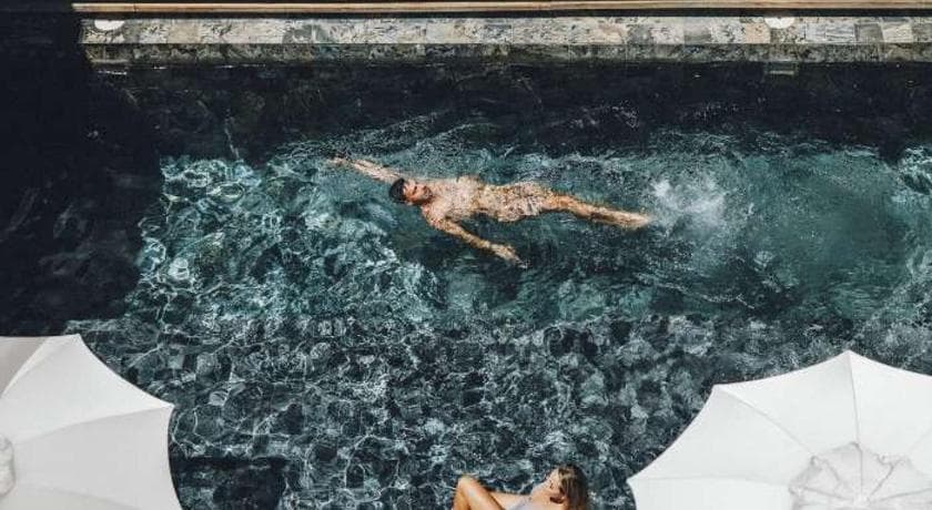 Nageur dans la petite piscine chauffée de l'Hôtel Le Saint-Pierre, vue plongeante sur l'eau et les parasols