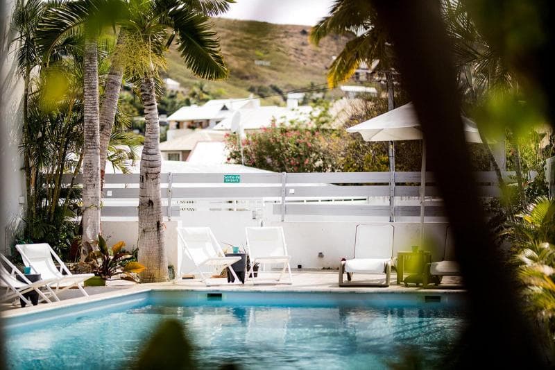 The pool at Hôtel Le Grand Bleu in Saint-Gilles, white sunloungers and palms with hillside houses behind