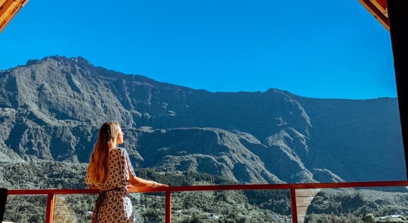 A guest on the terrace at Téréva Lodge in Cilaos, facing the cirque walls under a blue sky