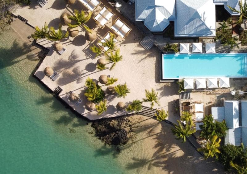 Vue aérienne du Veranda Grand Baie : ponton en bois planté de palmiers au bord de l'eau, piscine et toits blancs