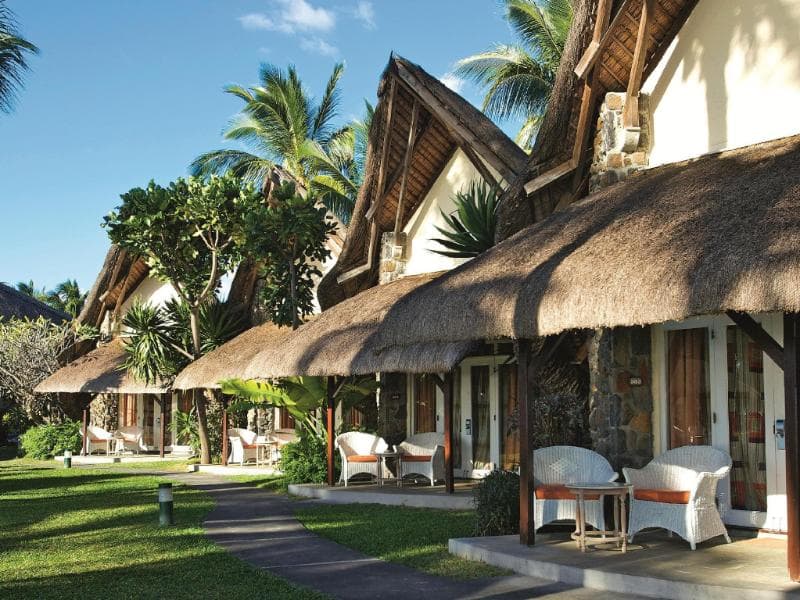 Bungalows au toit de palme de La Pirogue, terrasses et fauteuils blancs sur une pelouse sous les cocotiers
