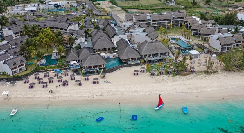 C Mauritius vu du ciel : plage avec parasols, catamaran à voile rouge et bâtiments à toits de chaume