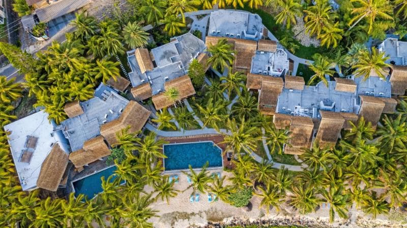 Seasense vu du ciel : bâtiments aux toits bleus et de chaume dans les cocotiers, deux piscines