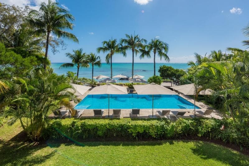 The rectangular pool at Mon Choisy Beach R framed by lawn and palm trees, with the sea behind