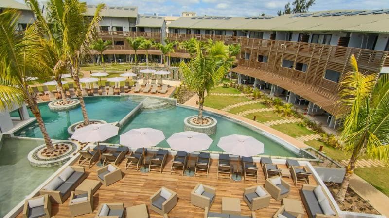 The curved pool at Be Cosy between modern three-storey buildings, with a wooden deck and parasols